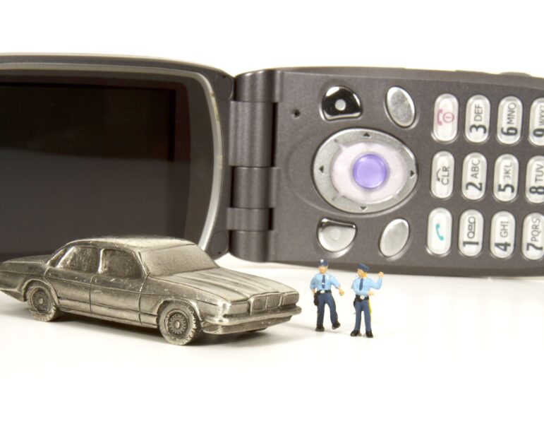 Cell phone and car with two people standing near it.